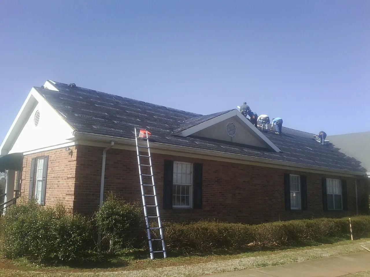 Crew tearing shingles off a brick ranch roof with a ladder set — Metal Roof Repair work by our crew in Esmont
