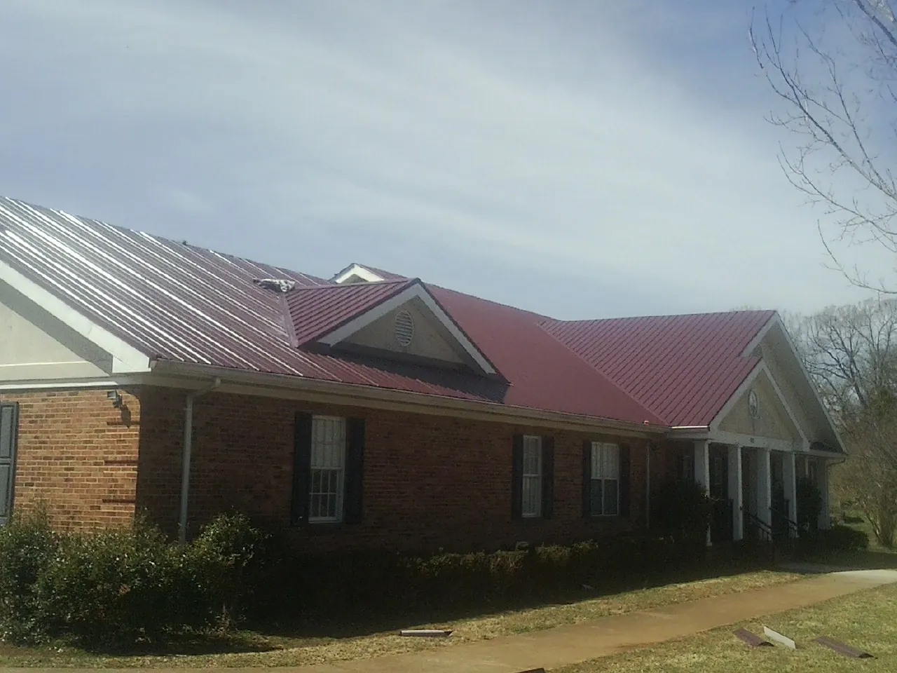 Red metal roof with gabled entries on a long brick building, from a Hail Damage Roof Repair job in Esmont