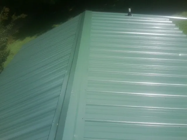 New green metal panels meeting at the ridge of a roof — Flat Roof Repair work by our crew in Esmont