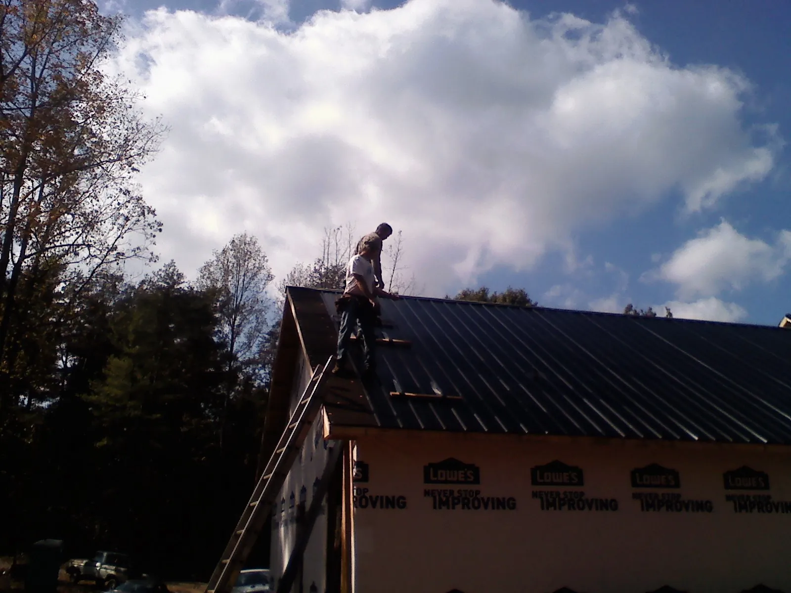 Roofer fastening dark metal panels high against a cloudy sky, from a Roof Inspection job in Esmont
