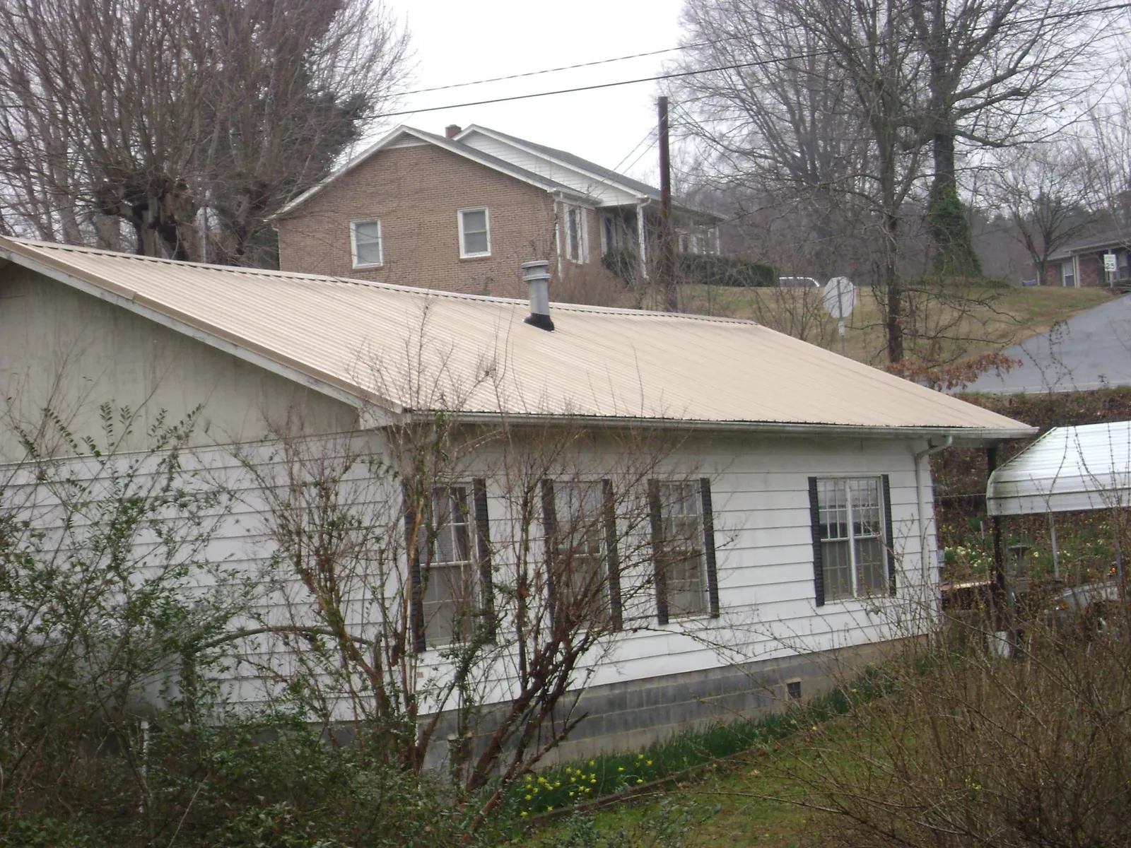 Tan metal roof on a white sided house set into a hillside — Commercial Roofing by Roofing Brothers in Esmont