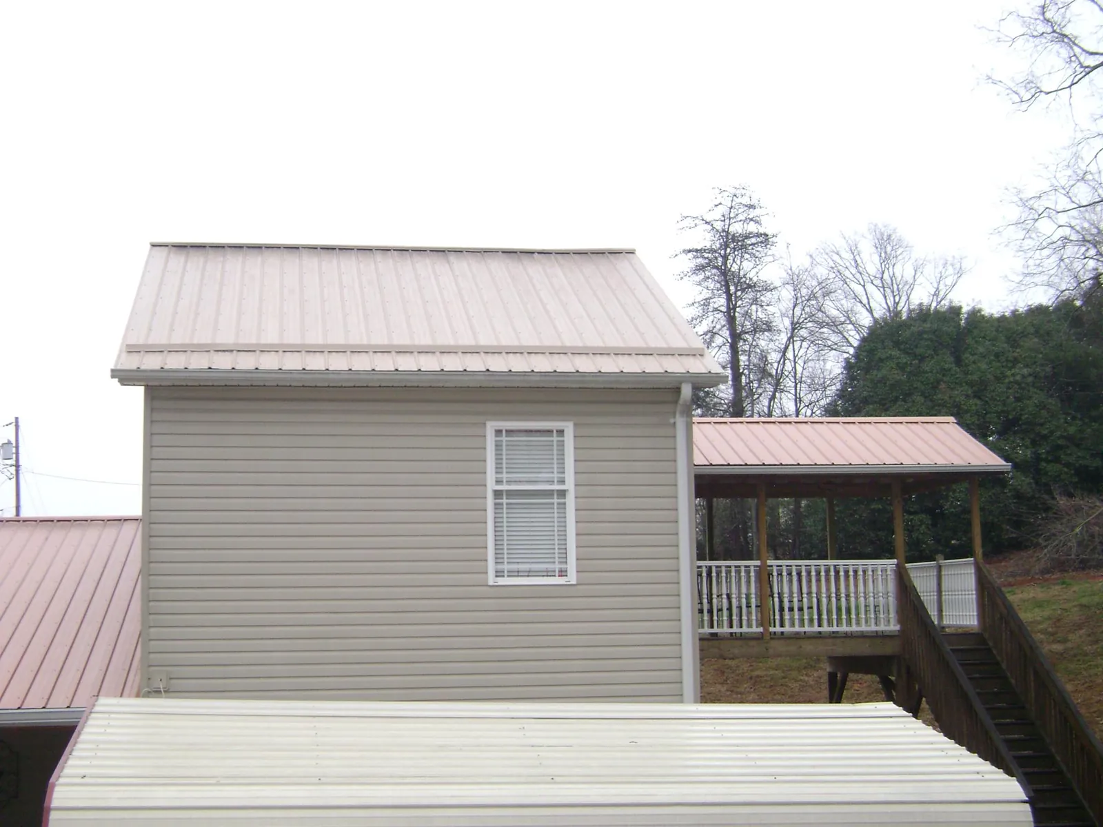 Tan metal roofs on a two story addition and attached porch, from a Roof Replacement job in Esmont